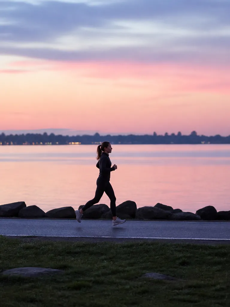 Kvinna som joggar längs vattnet i gryningen